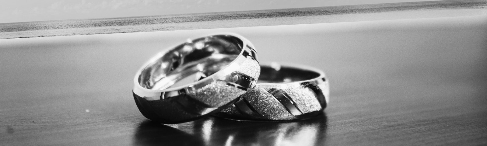 Deux alliances entrelacées posées sur une surface brillante, en arrière-plan une plage et l’océan, symbole d’union éternelle, par l’Agence Moment de Grâce.