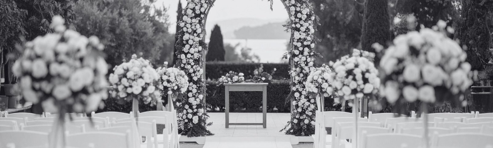 Vue d’une allée de cérémonie laïque décorée de fleurs blanches avec une arche florale centrale, en extérieur, ambiance élégante en noir et blanc – mariage organisé par l’Agence Moment de Grâce en Bretagne.