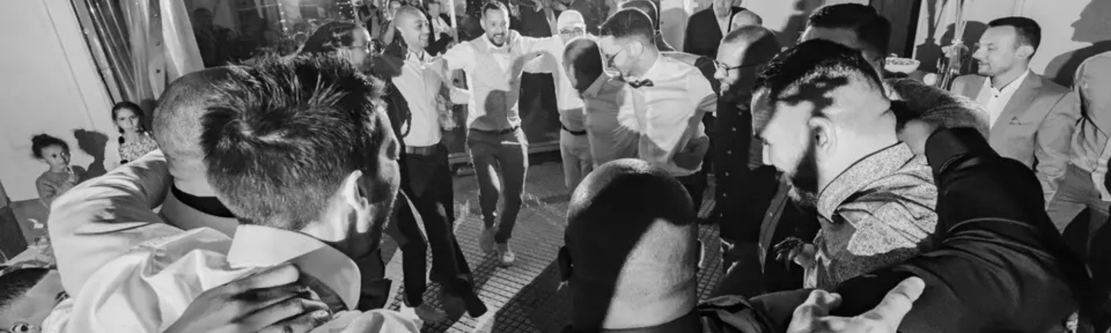 Groupe d’invités formant une ronde sur la piste de danse lors d’une soirée de mariage, ambiance festive en noir et blanc.