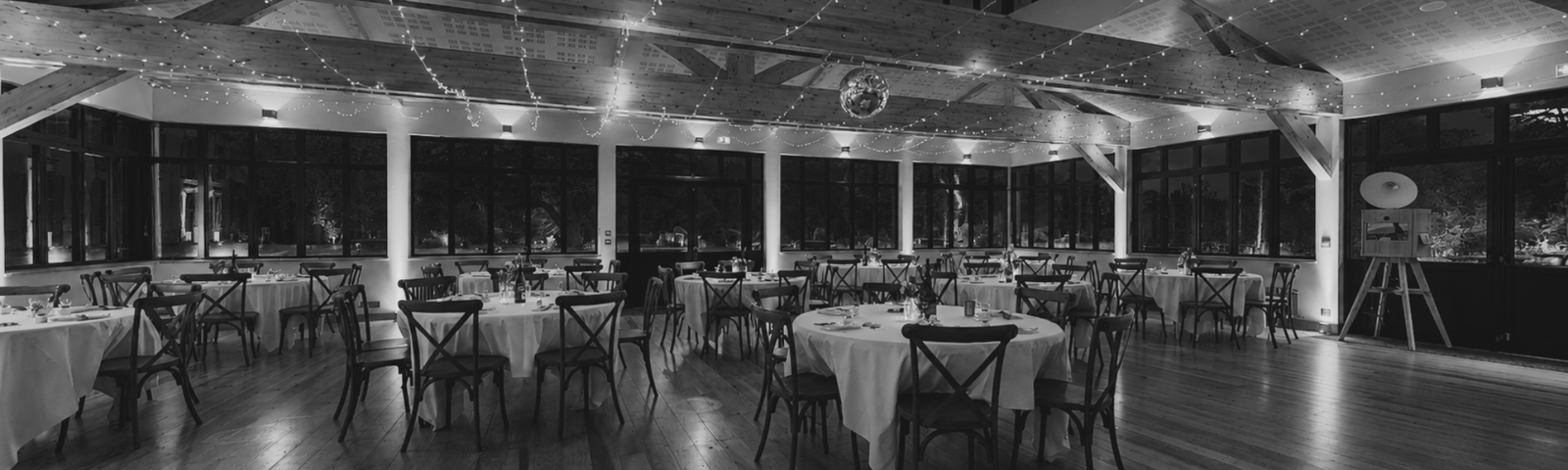 Salle de réception de mariage en Bretagne avec éclairage d’ambiance, tables rondes dressées et décoration élégante pour une réception organisée par l’Agence Moment de Grâce.