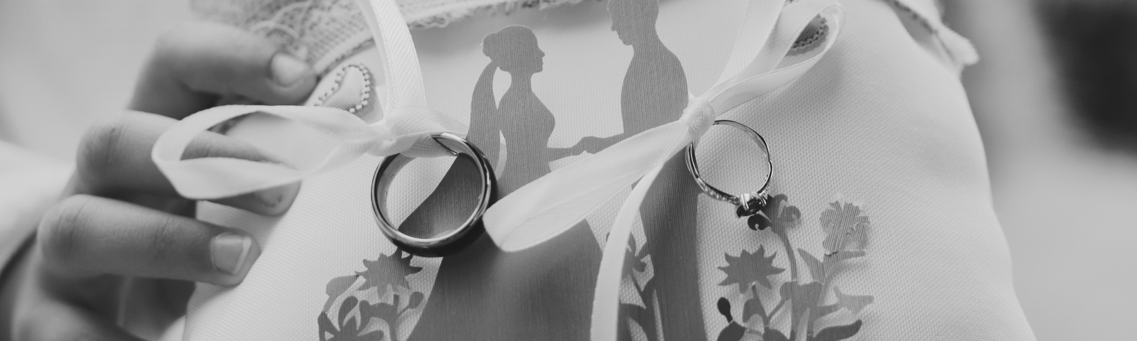 Alliances de mariage posées sur un porte-alliances personnalisé représentant un couple de mariés lors d'une cérémonie laïque en Bretagne.